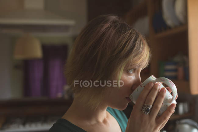 Beautiful woman having cup of coffee in kitchen at home — Stock Photo