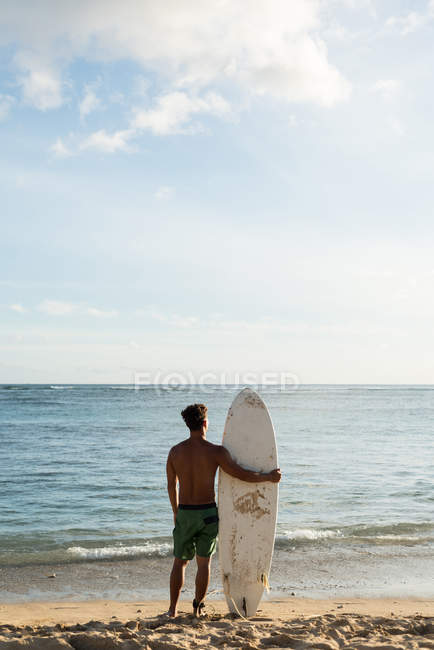 Rückansicht männlicher Surfer, der mit Surfbrett im Strand steht — Stockfoto