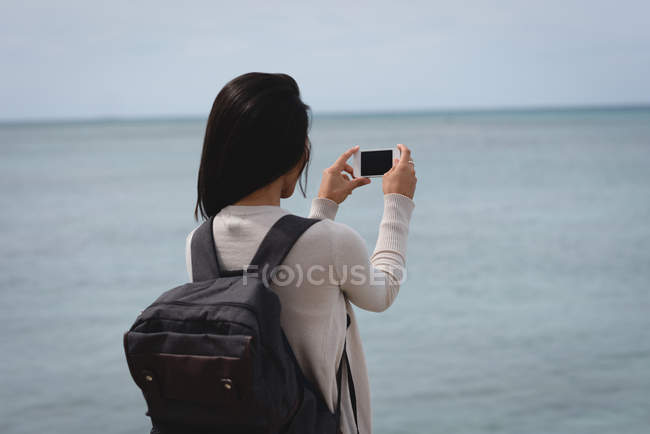 Vue arrière de la femme en cliquant sur la photo de la mer avec téléphone portable — Photo de stock
