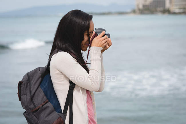 Vista laterale della donna che fotografa con fotocamera digitale in spiaggia — Foto stock