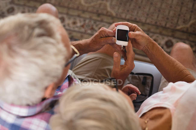Senior couple checking blood sugar with glucometer in living room at home — Stock Photo