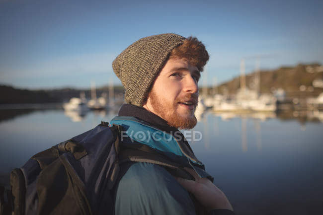 Молодий чоловічий пішохід стоїть з рюкзаком біля озера — стокове фото
