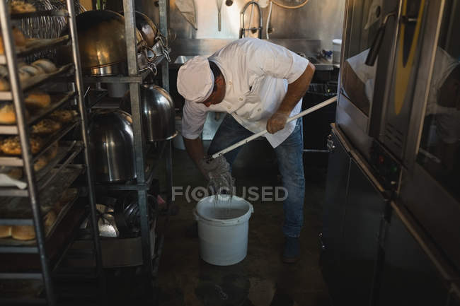 Male baker cleaning floor with floor mop in bakery shop — Stock Photo