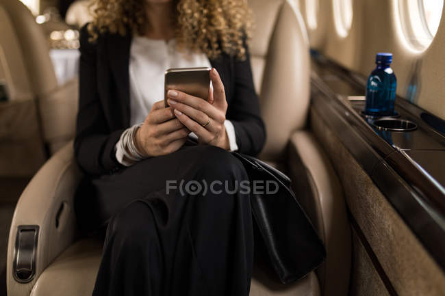 Partie médiane de la femme d'affaires utilisant le téléphone mobile en jet privé — Photo de stock