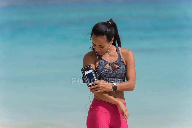 Femme écoutant de la musique sur un téléphone portable à la plage par une journée ensoleillée — Photo de stock