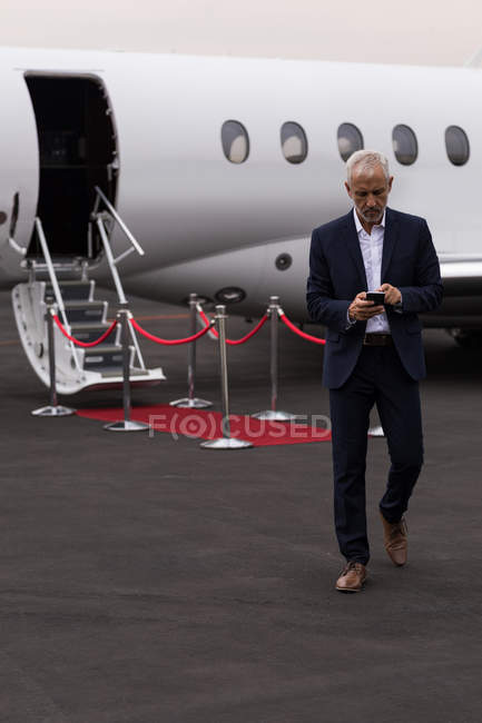 Старший бізнесмен, використовуючи мобільний телефон, залишаючи приватний літак — стокове фото