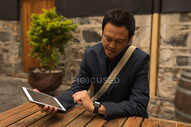 Усміхнений бізнесмен дивиться на смарт-годинник у тротуарному кафе — стокове фото