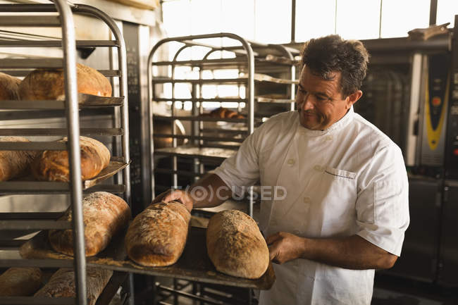 Чоловічий пекар перевіряє запечений хліб у хлібобулочній майстерні — стокове фото