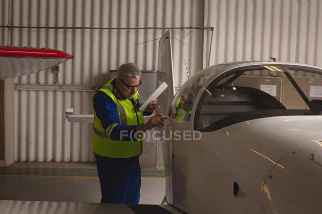 Ingeniero examinando parte de la aeronave en hangar aeroespacial - foto de stock