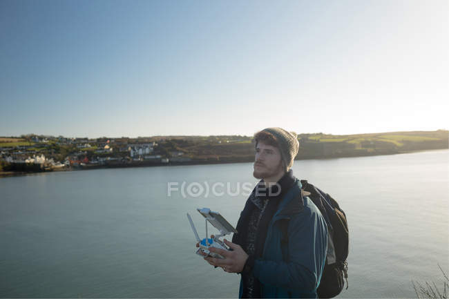 Male hiker operating drone near lake at countryside — Stock Photo