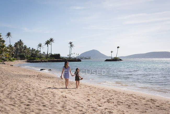 Vista trasera de la madre y la hija caminando juntas en la playa - foto de stock