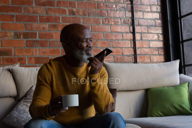 Homem sênior tomando café enquanto falava no celular em casa — Fotografia de Stock