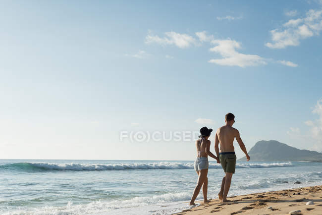 Coppia che cammina insieme mano nella mano sulla spiaggia — Foto stock