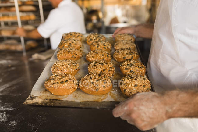 Mid section of male baker holding tray of baked sweet foods — Stock Photo