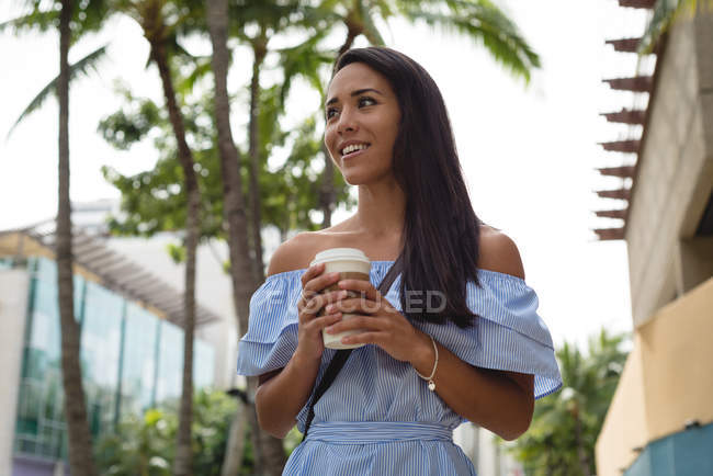 Улыбающаяся красивая женщина держит чашку кофе на улице — стоковое фото