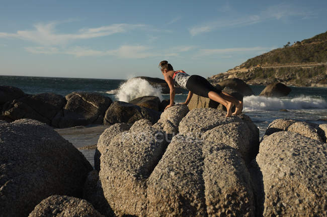Female volleyball player performing push up exercise on a rock at beach — Stock Photo