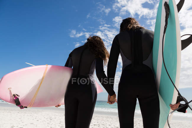 Rückansicht eines Surfer-Paares, das sich am Strand an den Händen hält — Stockfoto