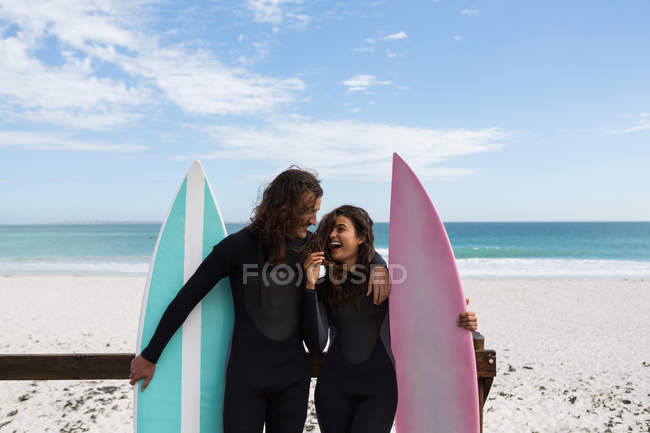 Pareja de surfistas de pie con tabla de surf en la playa en un día soleado - foto de stock