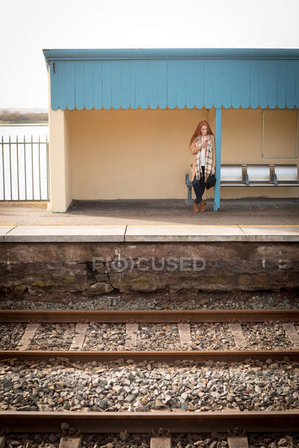 Mulher usando telefone celular na estação ferroviária em um dia ensolarado — Fotografia de Stock