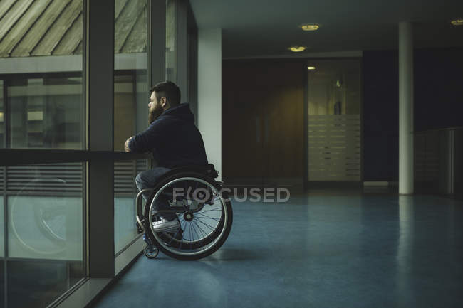 Side view of handicapped man on wheelchair looking out from glass pane — Stock Photo