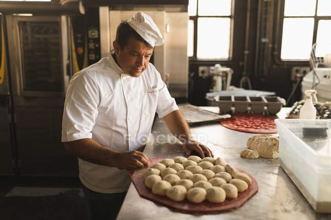 Зрелый мужчина-пекарь с тестовыми шариками в пекарне — стоковое фото