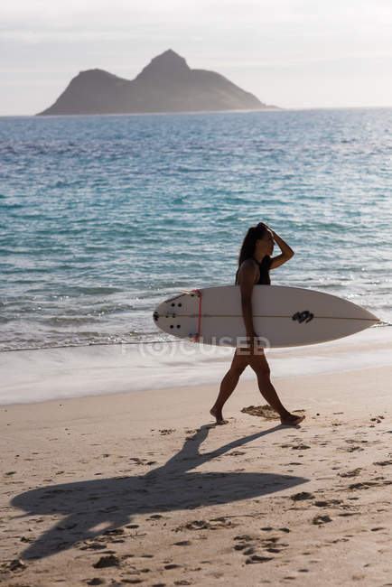 Donna che cammina con la tavola da surf in spiaggia in una giornata di sole — Foto stock