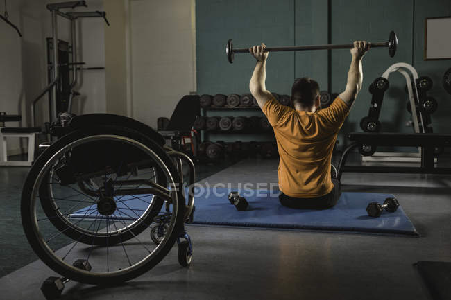 Rear view of handicapped man exercising with barbell in gym — Stock Photo
