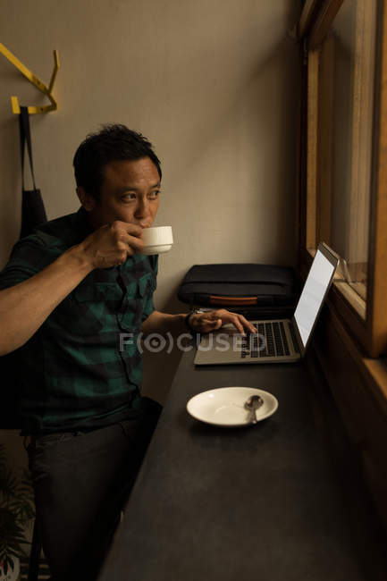 Empresário usando laptop enquanto toma café no café — Fotografia de Stock