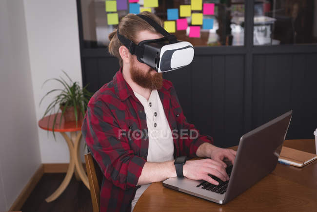 Чоловік виконавчий використовує гарнітуру віртуальної реальності з ноутбуком за столом в офісі — стокове фото