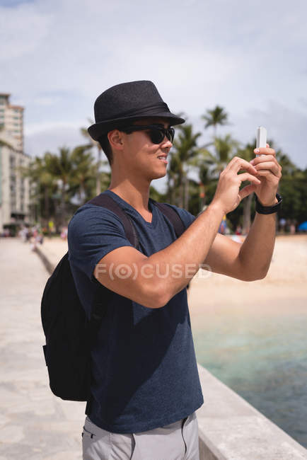 Homem clicando foto com telefone celular perto da praia — Fotografia de Stock