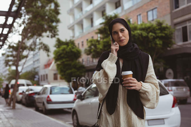 Hijab mulher falando no celular enquanto toma café na calçada — Fotografia de Stock
