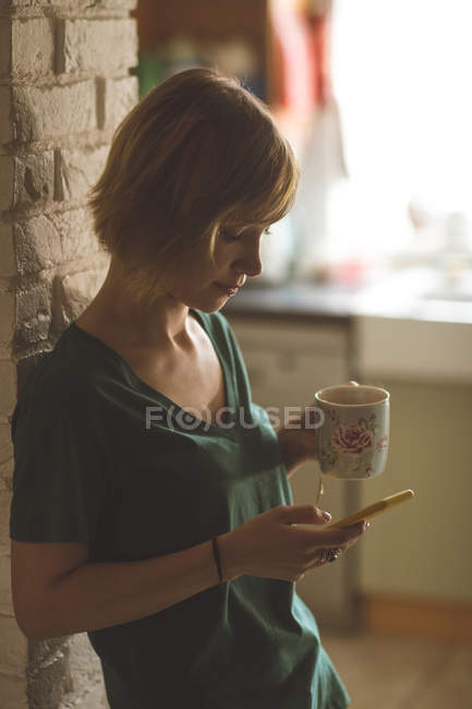 Красива жінка використовує мобільний телефон, маючи каву вдома — стокове фото