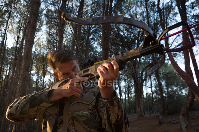 Uomo che punta il tiro con l'arco nella foresta con arco e freccia in una giornata di sole — Foto stock