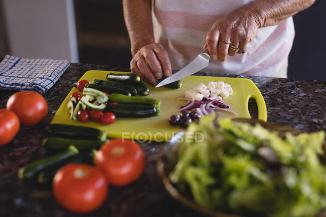 Partie médiane de la femme âgée coupant des légumes dans la cuisine à la maison — Photo de stock