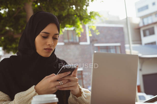 Hermosa mujer hijab utilizando el teléfono móvil en la cafetería del pavimento - foto de stock