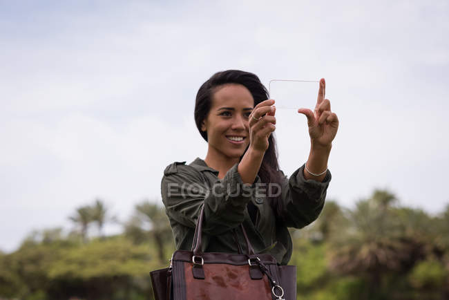 Mujer sonriente usando el teléfono móvil de vidrio en el parque - foto de stock