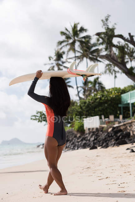 Женщина ходит с доской для серфинга на пляже в солнечный день — стоковое фото