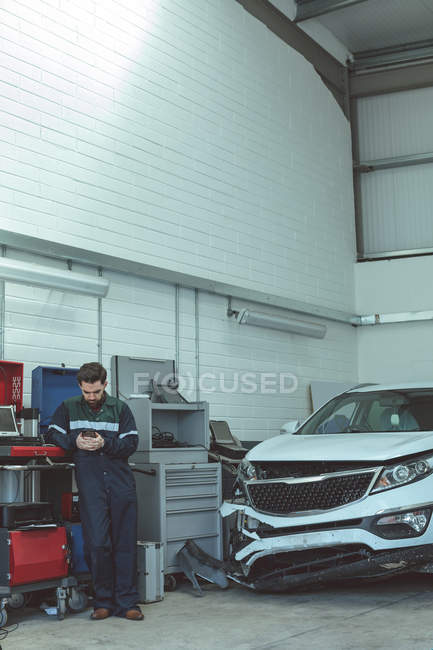 Mechanic using mobile phone while repairing car in the garage — Stock Photo