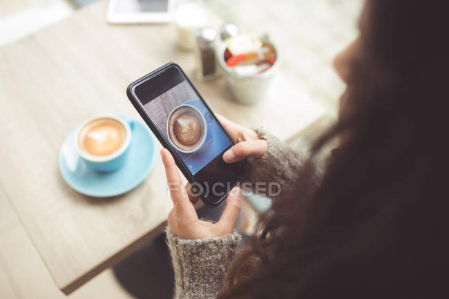 Mujer haciendo clic en la foto de café con teléfono móvil en la cafetería - foto de stock