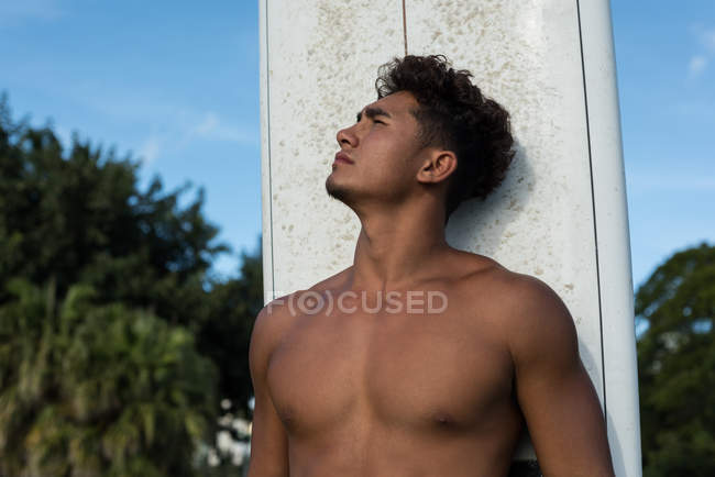Junger Mann steht mit Surfbrett am Strand — Stockfoto