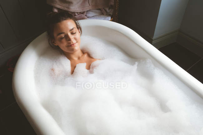 Mulher tomando um banho de espuma no banheiro em casa — Fotografia de Stock