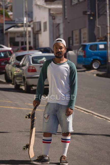 Portrait of man standing with skateboard in street — Stock Photo