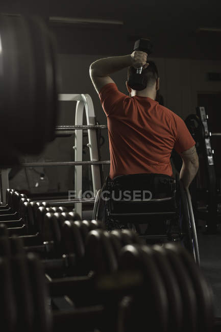 Hombre discapacitado en silla de ruedas haciendo ejercicio con mancuerna en el gimnasio - foto de stock