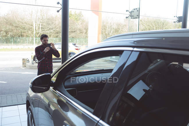 Vendeur prenant une photo de voiture avec téléphone portable au showroom — Photo de stock