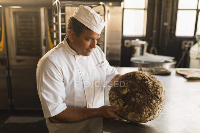 Panadero masculino examinando una masa en una panadería - foto de stock