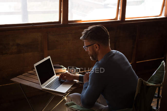 Homme utilisant un ordinateur portable à la table dans la cabane en bois rond — Photo de stock