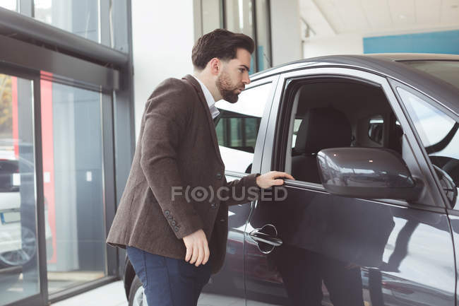 Handsome salesman examining car at showroom — Stock Photo