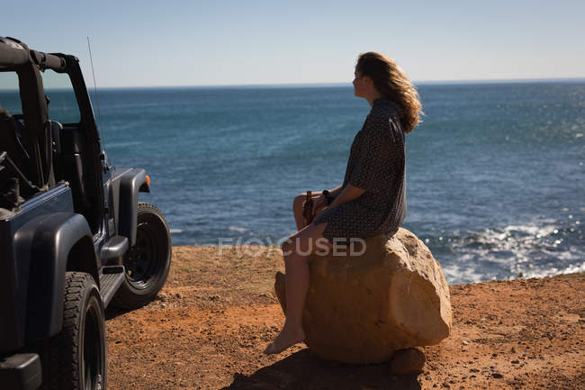 Nachdenkliche Frau sitzt auf einem Felsen am Strand — Stockfoto