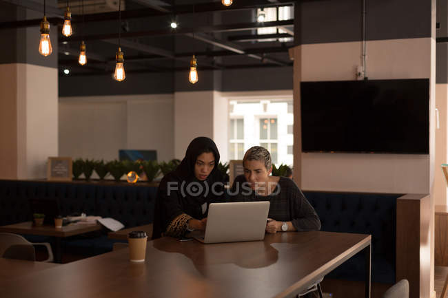 Collèges d'affaires utilisant un ordinateur portable à la cafétéria au bureau — Photo de stock