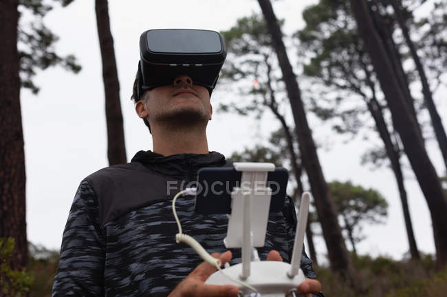 Людина, що керує літаючим безпілотником, використовуючи гарнітуру віртуальної реальності в сільській місцевості — стокове фото